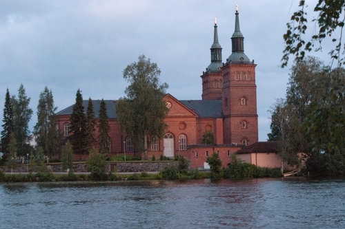 Kaksitorninen, punatiilinen Tyrvään kirkko järveltä päin kuvattuna.