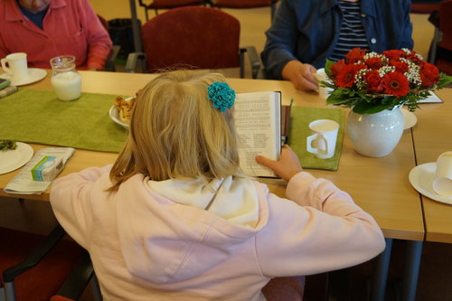Nuori tyttö lukee virsikirjaa kahvipöydän äärellä.