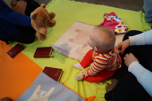 Lastenohjaaja esittelee lattialla istuvalle vauvalle nallepehmolelua.