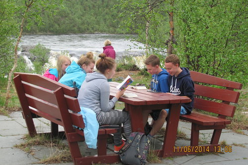 Joukko nuoria istumassa pihapenkeillä pöydän ääressä ja lukemassa.