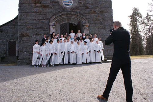 Valokuvaaja ottaa kuvan kirkon edessä seisovasta konfirmoitujen nuorien ryhmästä. 