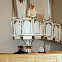 Pastori Hannu Heikkilä seisomassa saarnatuolissa.