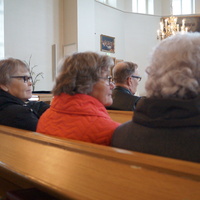 Kirkon väkeä istumassa penkissä ja kuuntelemassa puhujia.