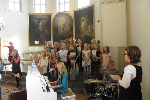 Lapsikuoro laulaa Tyrvään kirkon alttarialueella pianon, rumpujen ja viulun säestämänä.